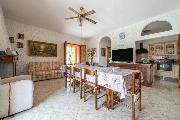 A dining area with a table set for six, a sofa, a television, and a kitchen in the background.