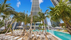 Un hotel moderno con un amplio espacio de piscina rodeado de palmeras y tumbonas.