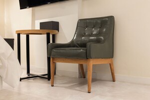 Una habitación moderna con un sillón de cuero, una mesita redonda y un televisor de pantalla plana montado en la pared.