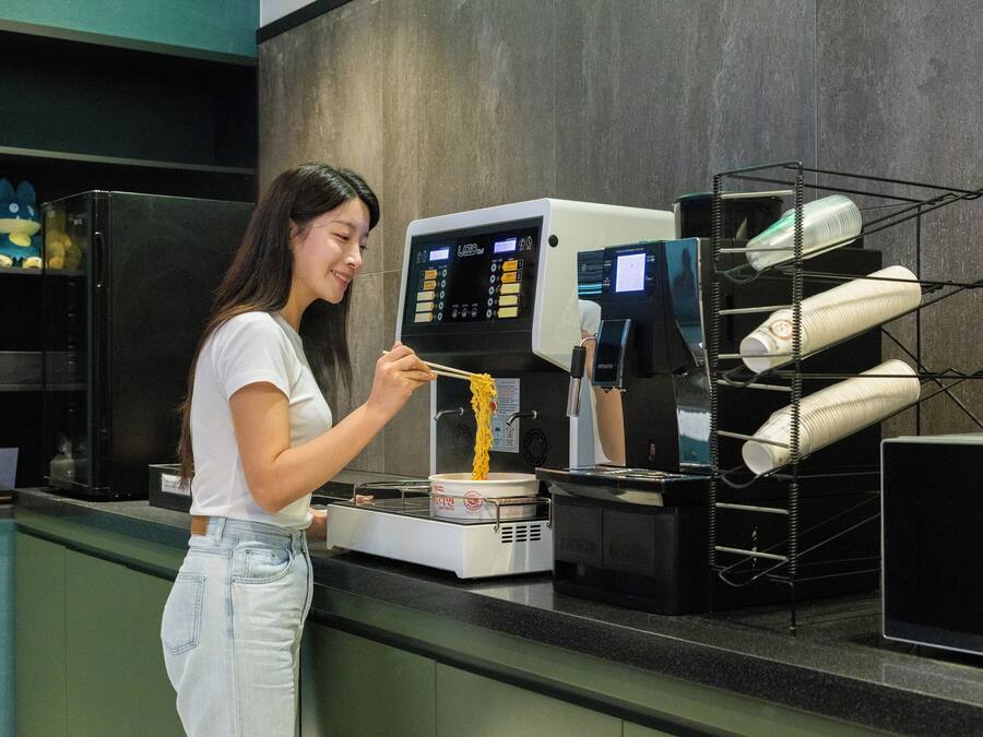 A person preparing food in a kitchen with a commercial cooking appliance and a metal rack with paper products.
