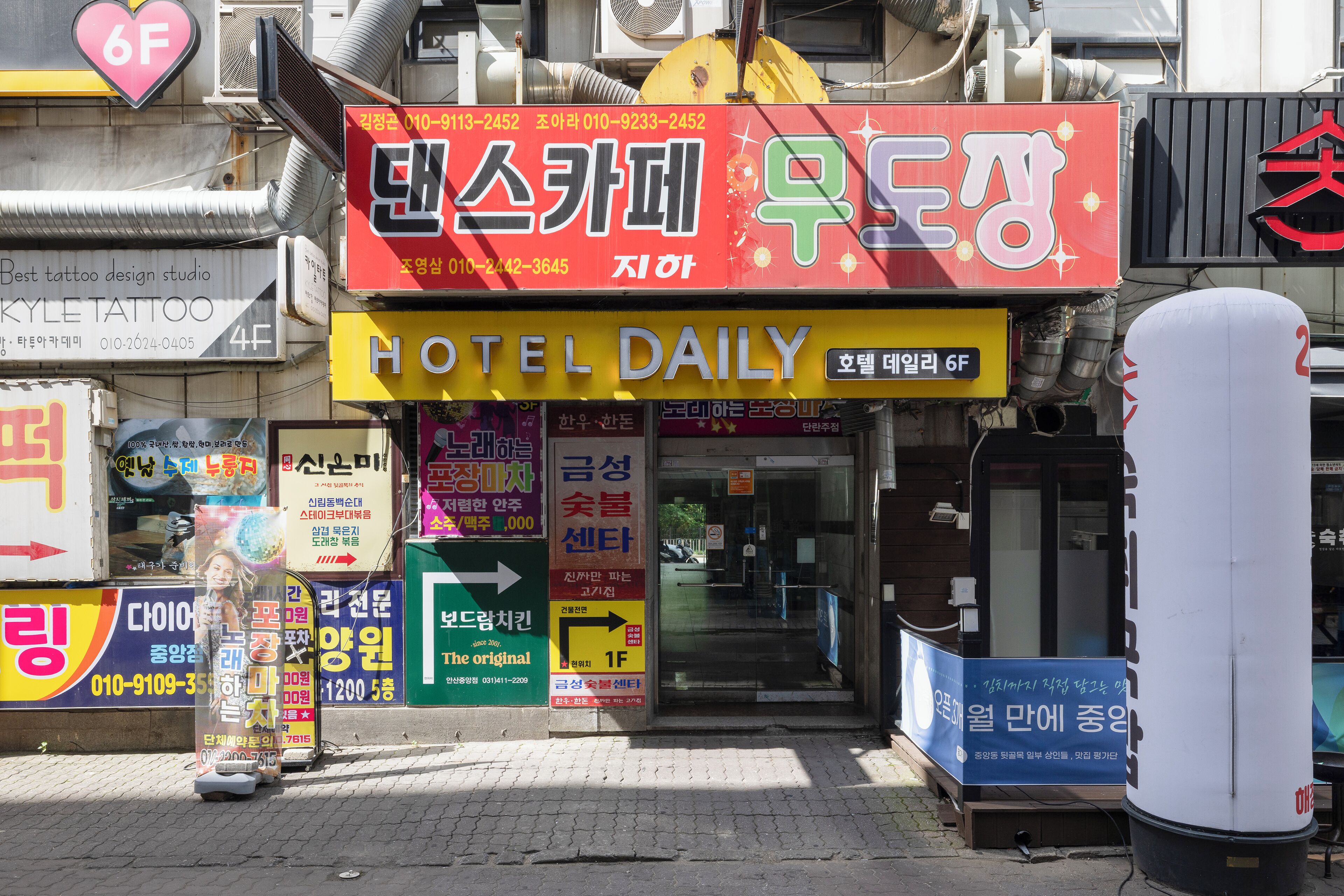 A hotel entrance with multiple signs, including a prominent 'HOTEL DAILY' sign and various directional and informational signs.