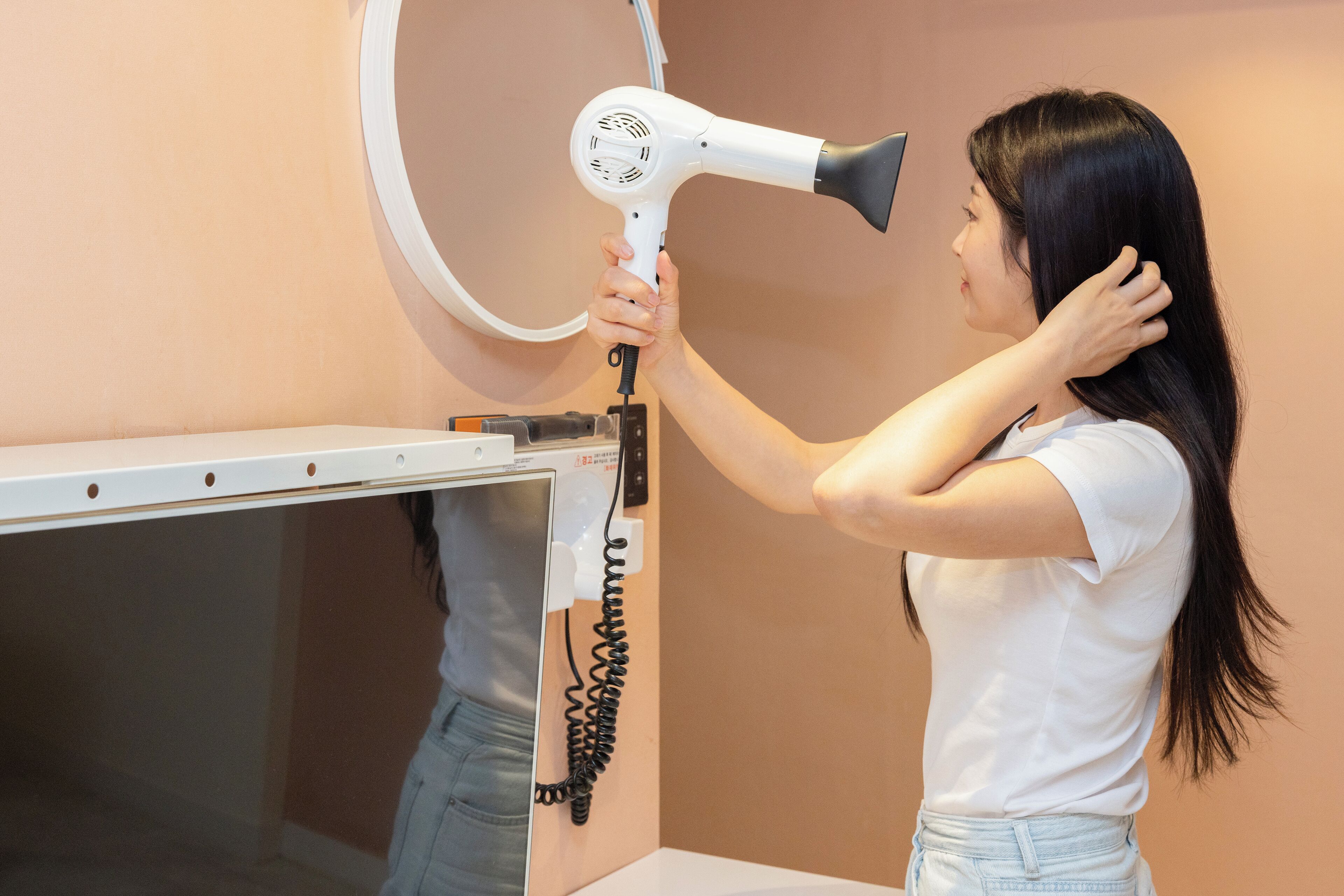 A person using a hair dryer in a room with a white wall and a white counter.