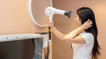 A person using a hair dryer in a room with a white wall and a white counter.
