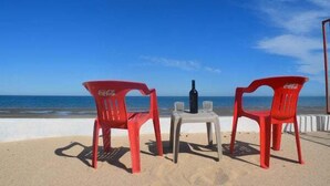 Un cadre idyllique sur la plage, avec deux chaises rouges, une petite table et une bouteille, le tout offrant une vue sur l’océan.