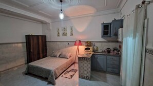 A bedroom with a bed, a wardrobe, a desk with a lamp, a kitchen area, and a bathroom with a shower curtain. - Studio with terrace 10 mn from airport and beach sablette beatch (El-Harrach)
