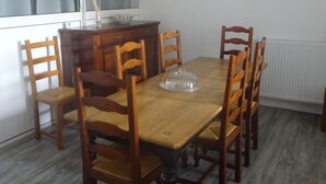 Une salle à manger avec une table et des chaises en bois, un vase contenant des plantes séchées, une horloge au mur et une fenêtre avec des rideaux.