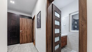 Un pasillo con puertas de madera oscura, suelo de baldosas y ventana con vista a edificios.