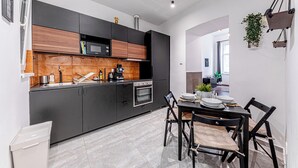 Una cocina moderna con armarios oscuros, un microondas y un horno. Hay una mesa de comedor con sillas y una planta en maceta.