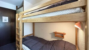 A bunk bed with a ladder, a bedside table, and a wall-mounted shelf.