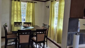 Un comedor con una mesa redonda, seis sillas y cortinas amarillas.
