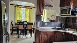 Una cocina con armarios de madera, un microondas y un comedor con sillas y una mesa.