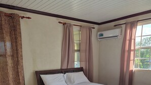 Una cama bien tendida con una toalla enrollada, cabecera de madera y una ventana con cortinas.
