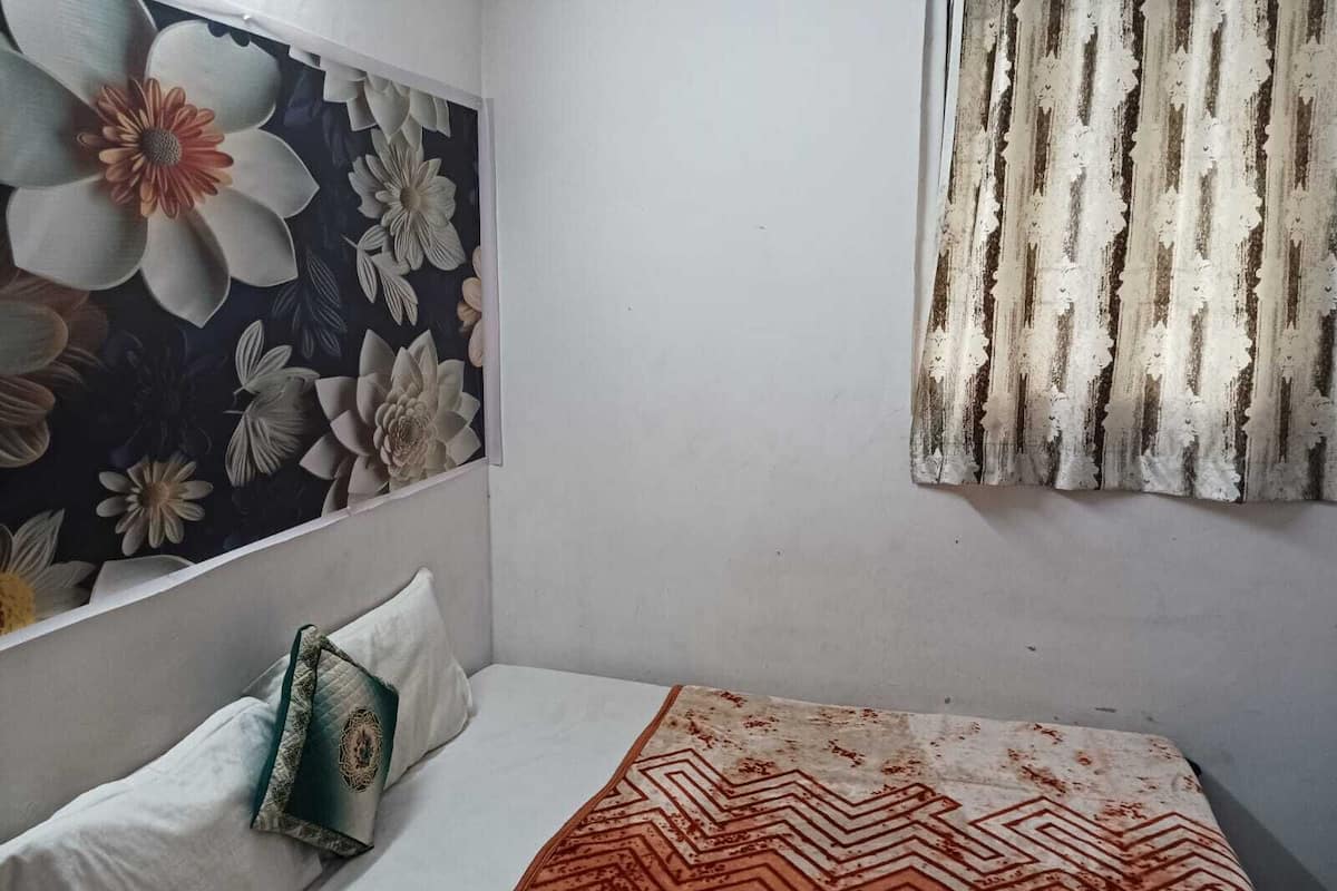 Ein Schlafzimmer mit einem Bett, einem Kopfkissen, einer Wand mit Blumenmuster und einem Vorhang.