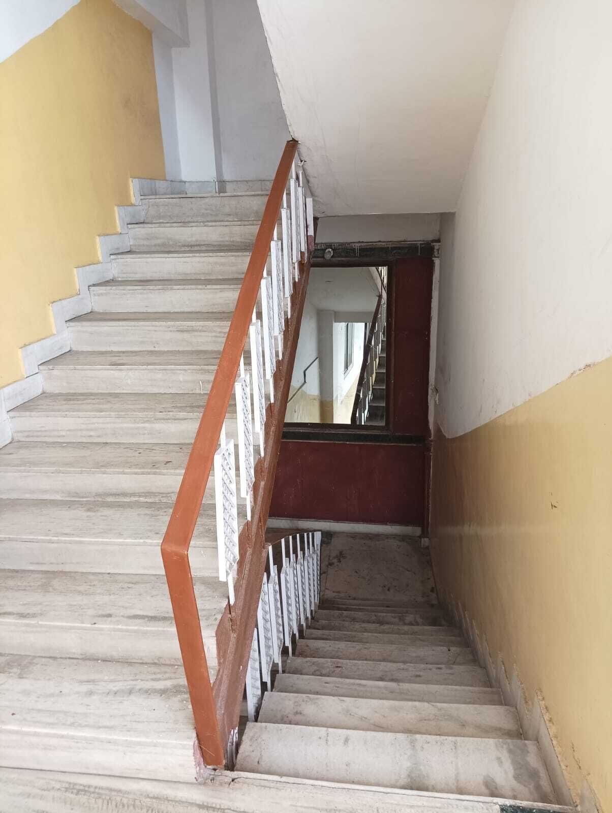 Una escalera con barandilla de madera y balaustres blancos que conduce a un rellano con una puerta roja.