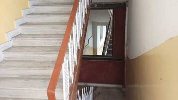 Una escalera con barandilla de madera y balaustres blancos que conduce a un rellano con una puerta roja.