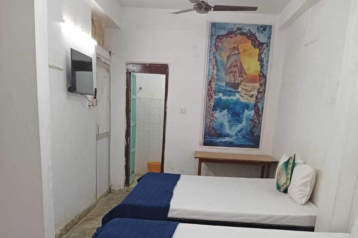 Ein Zimmer mit zwei Einzelbetten, einem Deckenventilator, einem Gemälde an der Wand und einem kleinen Tisch.