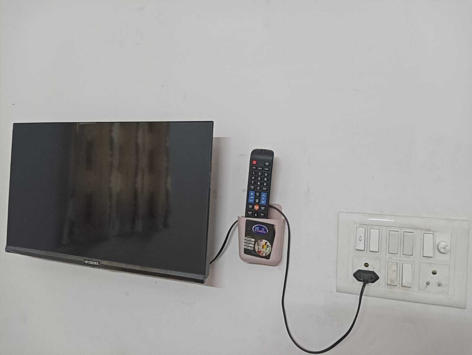 A flat-screen TV, a remote control, and a power outlet on a wall.