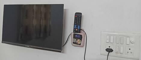 A flat-screen TV, a remote control, and a power outlet on a wall.