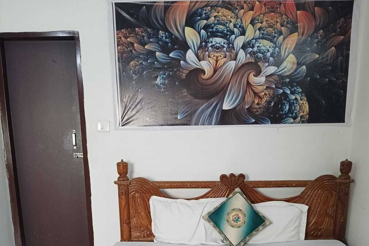 Ein Bett mit blumigem Überwurf, einem Zierkissen und einem Wandgemälde darüber.