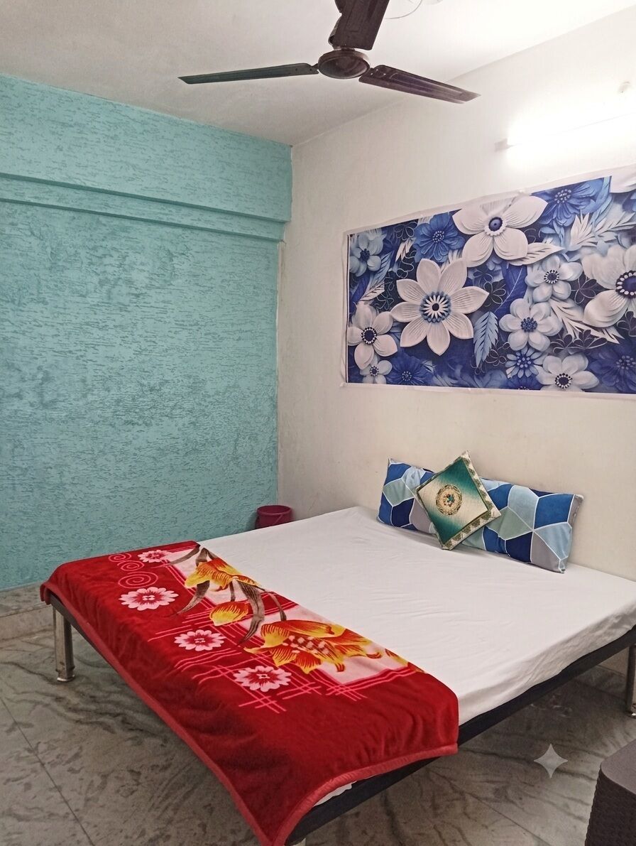 Une chambre à coucher avec un lit, un ventilateur de plafond, une tapisserie murale à motifs floraux et une couverture de lit rouge.