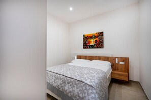 A bedroom with a bed, a wooden headboard, a nightstand, a wall-mounted painting, and a ceiling light.