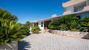 A modern two-story house with a paved driveway, surrounded by lush greenery and a stone wall. - Apartment 'L'Aia - 2' with Shared Pool, Wi-Fi and Air Conditioning (Monopoli)