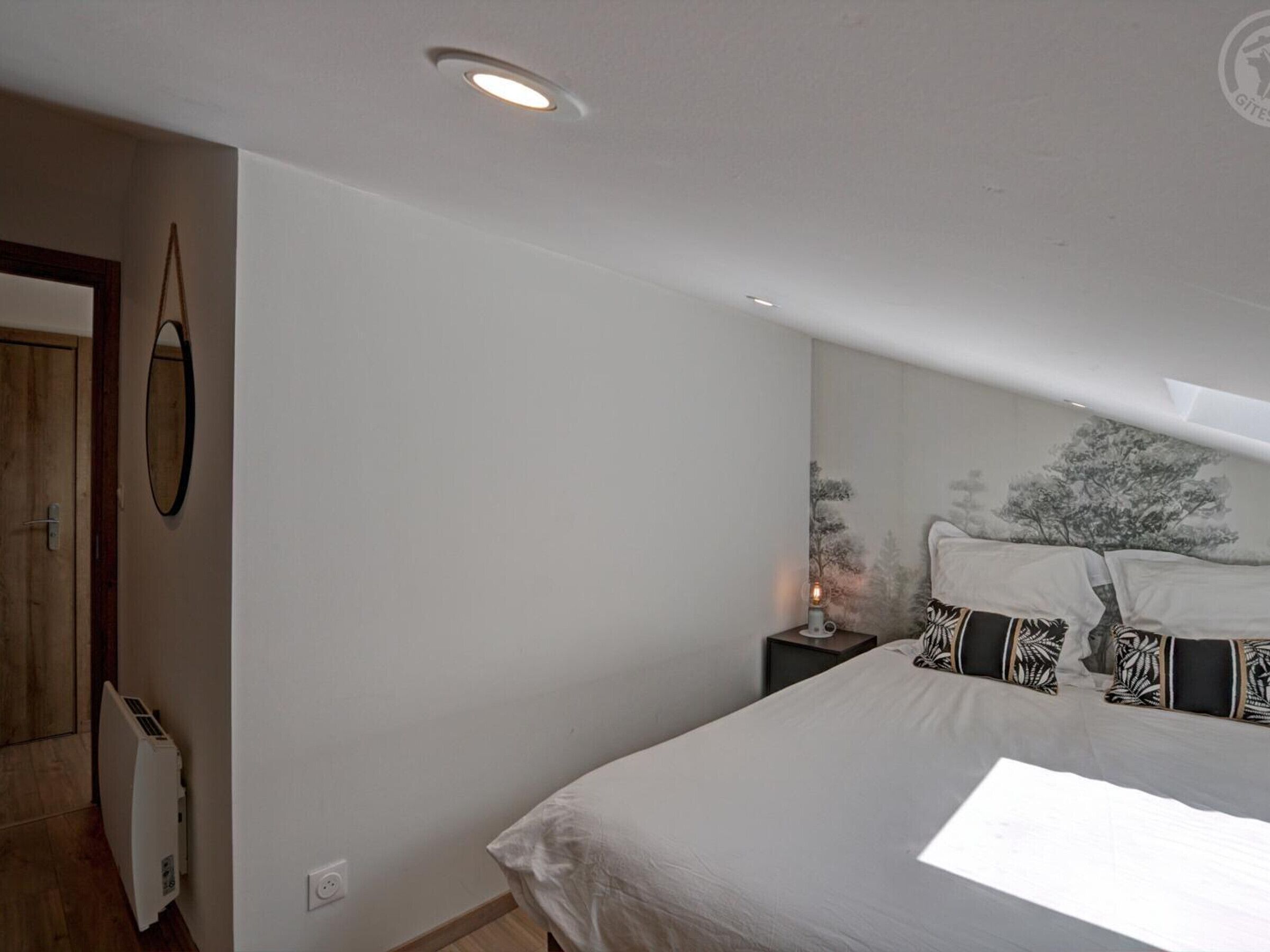 A bedroom with a bed, a nightstand, a wall-mounted mirror, and a radiator.