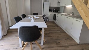 Eine moderne Küche mit weißen Schränken, einer Holztreppe und einem Essbereich mit weißem Tisch und Stühlen.