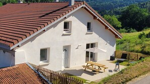 Ein zweistöckiges Haus mit rotem Ziegeldach, einer Holzterrasse und einem Picknicktisch mit Sonnenschirm.