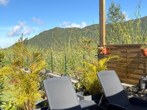 A patio area with two lounge chairs, a wooden fence, and a view of a mountainous landscape.