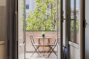 Un balcón con una mesa y sillas, una planta en maceta y vistas a árboles y edificios.