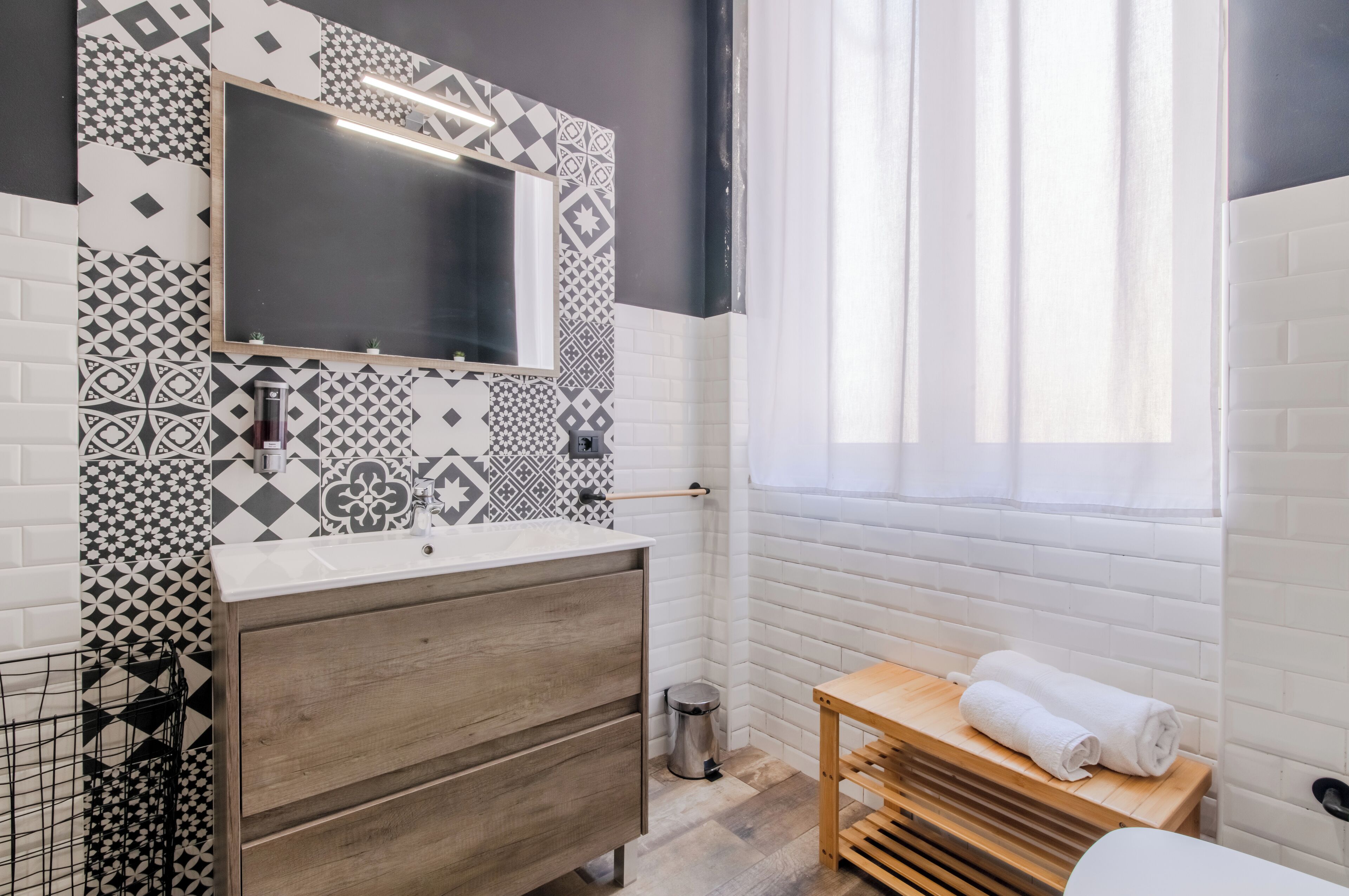Une salle de bain moderne avec des carreaux à motifs, un meuble-lavabo en bois, un miroir et une fenêtre avec des rideaux.