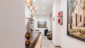 Un corridoio con una lunga panca di legno, una lampada in ottone e un quadro appeso al muro.
