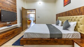 A modern bedroom with a wooden headboard, a large bed, a flat-screen TV, and a ceiling light fixture. - A radiant villa on the Ganges (Rishikesh)