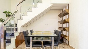 A dining area with a glass table and black chairs, a staircase with glass railings, and a wooden shelf unit against the wall. - A radiant villa on the Ganges (Rishikesh)