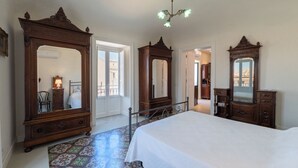 A bedroom with a large bed, two ornate wooden dressers, a chandelier, and a colorful tiled floor.