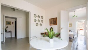 A dining area with a round white table and clear chairs, a potted plant, and decorative plates on the wall.
