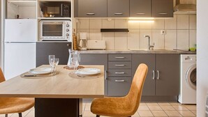 A modern kitchen with grey cabinets, a built-in oven, a microwave, and a coffee maker. There is a dining table with two chairs and a pitcher of water. - Calm T2 Apartment with Balcony and Wifi (Barbotan-les-Thermes)
