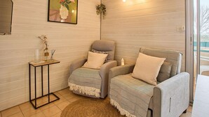 A modern room with two armchairs, a small side table, a framed floral artwork, and a glass door leading outside. - Calm T2 Apartment with Balcony and Wifi (Barbotan-les-Thermes)