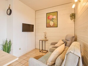 Uma sala de estar com sofá, mesinha lateral, televisão e um quadro na parede.