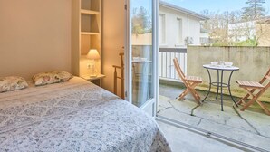 A bedroom with a bed, a nightstand, a lamp, and a view of the outside balcony with chairs and a table.