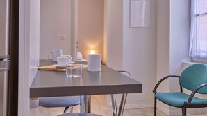 A modern dining area with a table set for two, a teal chair, and a refrigerator. - Charming renovated T2 in Barbotan, pets allowed, free parking and Wifi (Barbotan-les-Thermes)