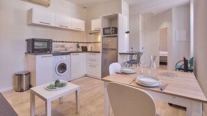 A compact kitchen with a washing machine, microwave, and a small dining table set for two. - Charming renovated T2 in Barbotan, pets allowed, free parking and Wifi (Barbotan-les-Thermes)