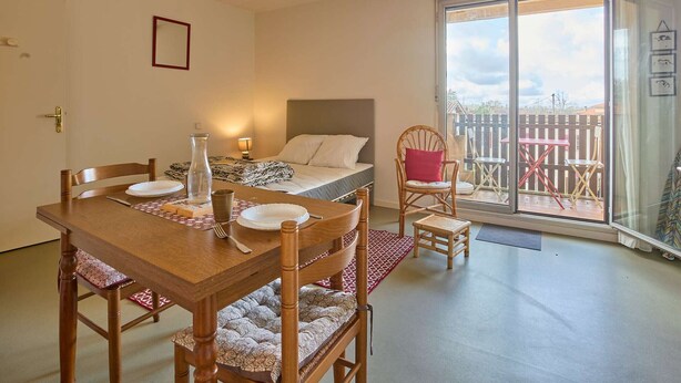 Une pièce chaleureuse avec une table à manger en bois, des chaises, un lit avec une tête de lit, une petite table avec des chaises à l’extérieur et un balcon avec vue.