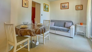 Un coin repas avec une table ronde, des chaises et un canapé. Il y a une horloge au mur et des tableaux encadrés.