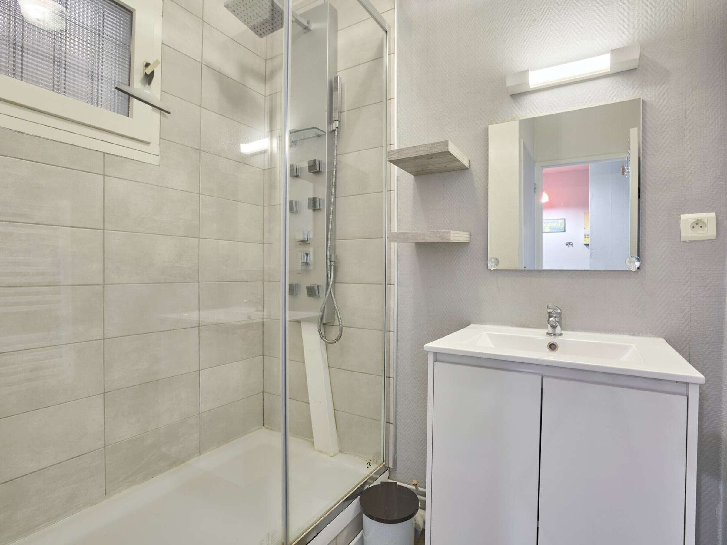 Une salle de bain moderne avec une douche à parois de verre, un lavabo blanc et un miroir au-dessus.