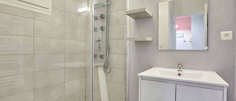 Une salle de bain moderne avec une douche à parois de verre, un lavabo blanc et un miroir au-dessus.