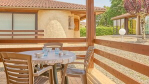 An outdoor patio with a round table and chairs, a wooden pergola, and a building with a tiled roof in the background. - T2 Apartment with Terrace - Pets Allowed in Barbotan-les-Thermes (Barbotan-les-Thermes)