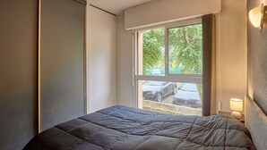 Une chambre à coucher avec un lit, une fenêtre avec des rideaux et une table de chevet avec une lampe.