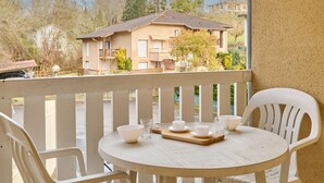 A balcony with a round table set for tea, white plastic chairs, and a view of a house with a sloped roof and a garden. - Quiet studio with Wifi and parking in Barbotan-les-Thermes (Barbotan-les-Thermes)